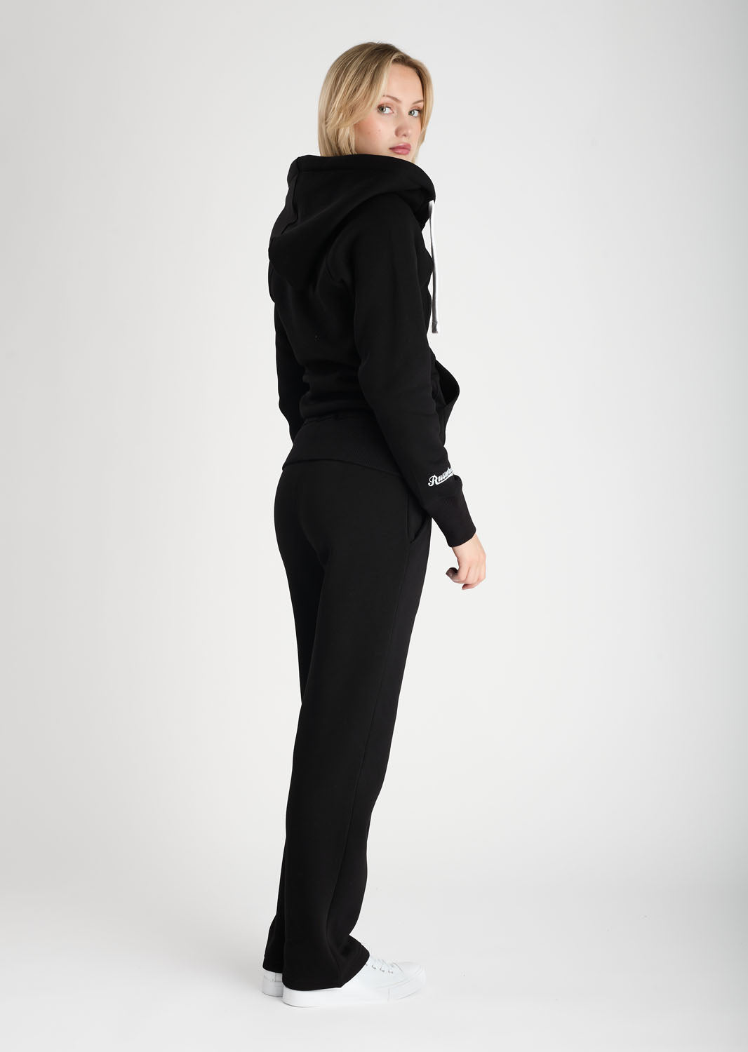 Person wearing a black hoodie and pants on a white background